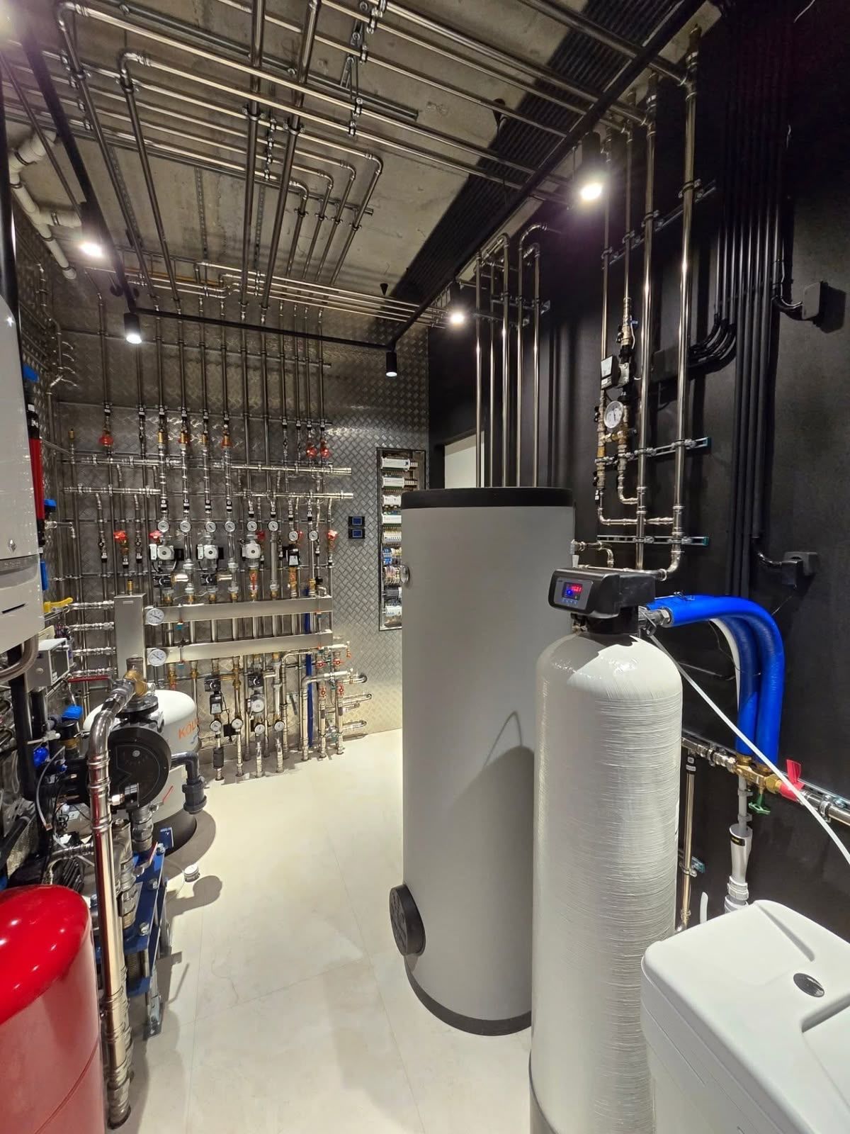 Technikraum mit Heizkreisverteiler und Pumpen, Rohrleitungen aus Edelstahl, Warmwasserspeicher und Enthärtungsanlage